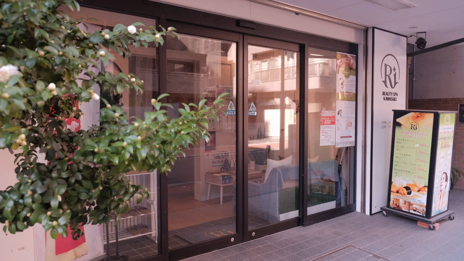 Ri Beauty Spa Kawasakiのロゴを掲げたガラス張りの入口と、脇に置かれた案内看板